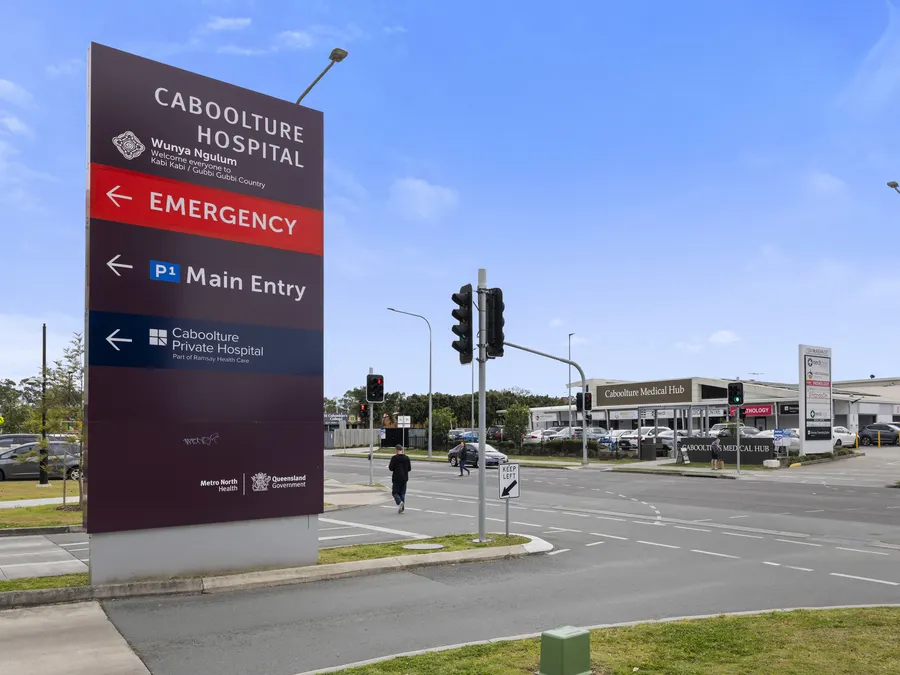 Caboolture Hospital's directional sign for Emergency, Main Entry and Caboolture Private Hospital at the McKean Street intersection, with Caboolture Medical Hub across the road