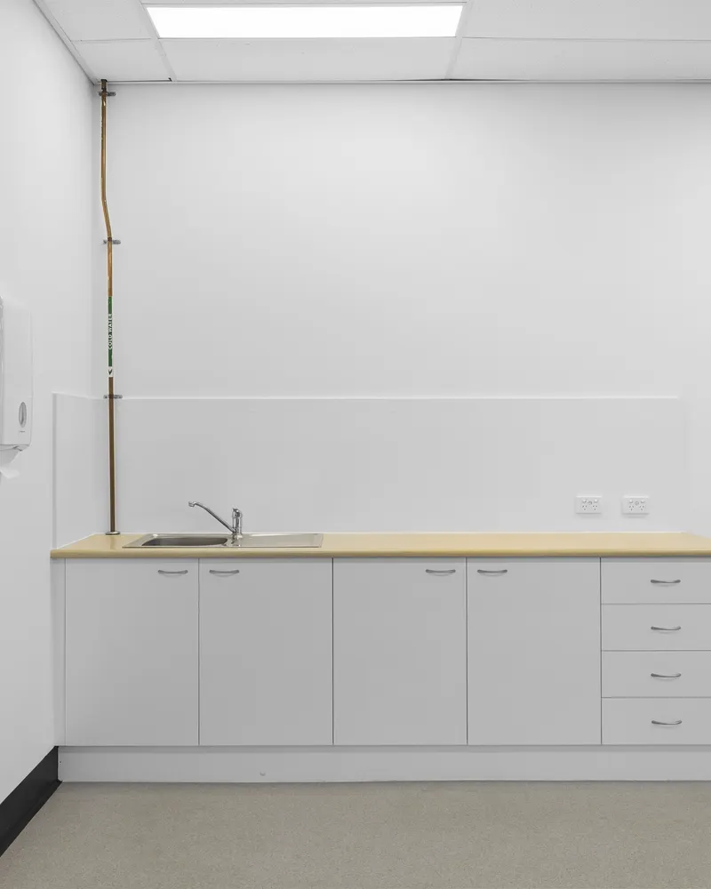 A kitchenette bench with a stainless sink, white cupboards and drawers inside a suite